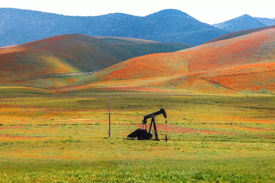 Abandoned oil well against hill covered in blooming orange flowers in Carrizo Plain National Monument, California.